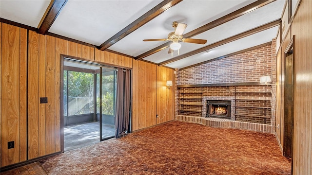 unfurnished living room featuring wood walls, vaulted ceiling with beams, dark carpet, a fireplace, and ceiling fan