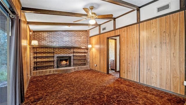 unfurnished living room with vaulted ceiling with beams, carpet floors, a brick fireplace, ceiling fan, and wooden walls