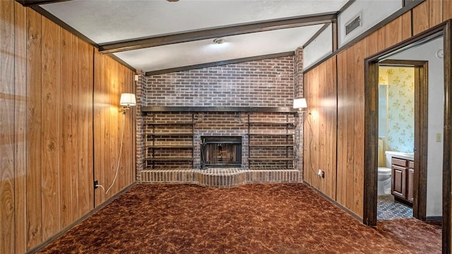 unfurnished living room with vaulted ceiling with beams, wood walls, dark carpet, and a brick fireplace