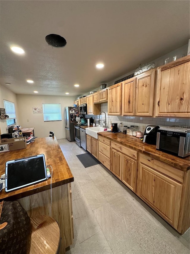 kitchen featuring wood counters, sink, decorative backsplash, light tile patterned floors, and stainless steel appliances