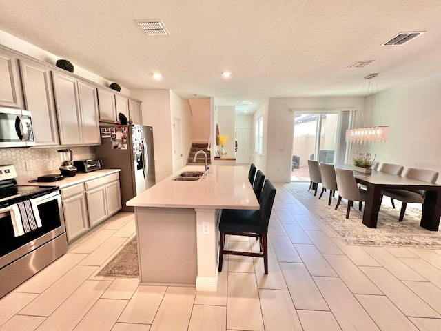 kitchen with appliances with stainless steel finishes, sink, an island with sink, pendant lighting, and a breakfast bar area