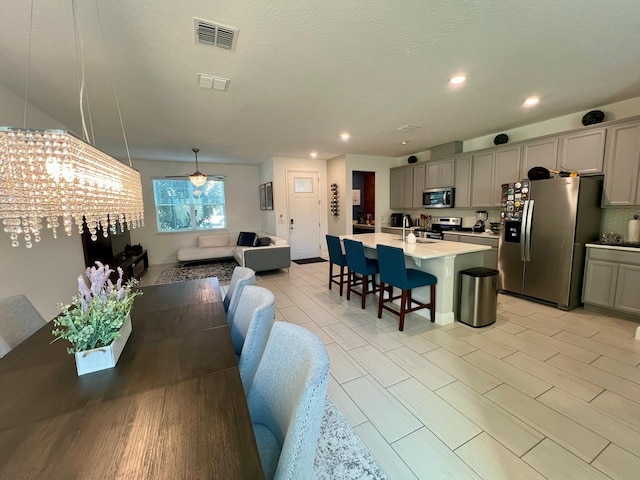 dining area with light hardwood / wood-style floors, a textured ceiling, sink, and ceiling fan with notable chandelier