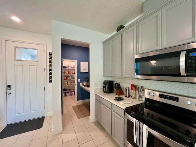 kitchen featuring decorative backsplash, light tile patterned floors, a textured ceiling, gray cabinets, and stainless steel appliances