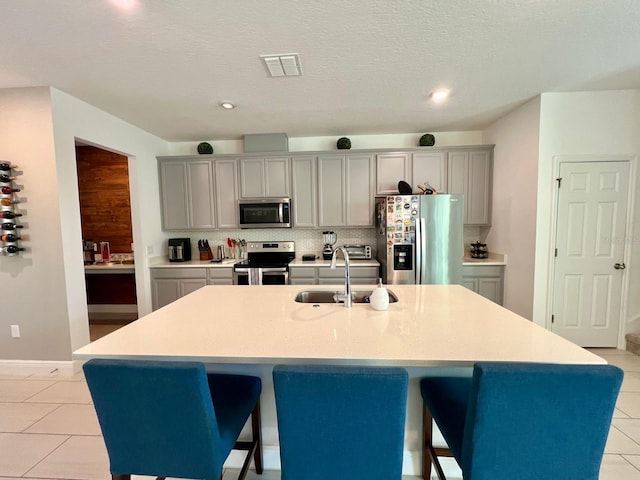 kitchen with gray cabinetry, stainless steel appliances, and an island with sink