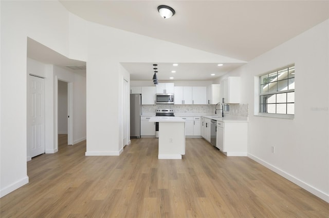 kitchen featuring lofted ceiling, a kitchen island, stainless steel appliances, light wood-type flooring, and white cabinetry