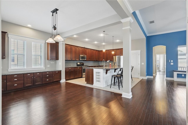 kitchen featuring a breakfast bar, pendant lighting, stainless steel appliances, visible vents, and an island with sink