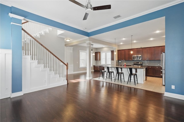 living room featuring ceiling fan, wood finished floors, visible vents, stairs, and ornamental molding