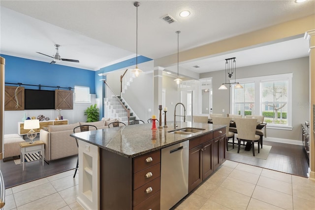 kitchen with visible vents, stainless steel dishwasher, open floor plan, a sink, and dark stone countertops