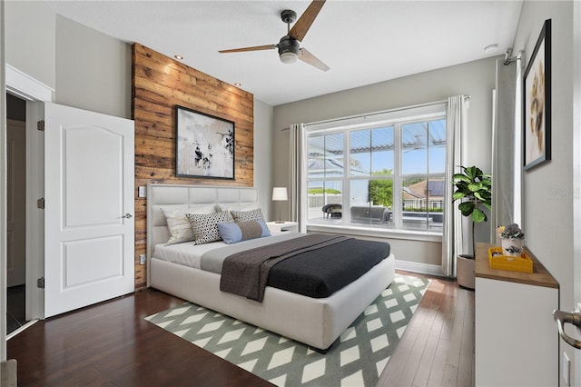 bedroom featuring dark wood-type flooring, an accent wall, wood walls, and ceiling fan