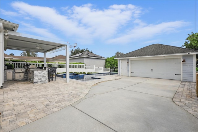 exterior space featuring an outdoor kitchen, a detached garage, fence, roof with shingles, and an outdoor bar