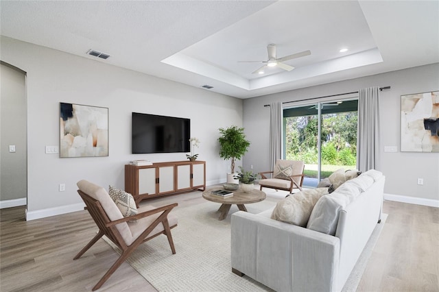 living room featuring a tray ceiling, ceiling fan, and light hardwood / wood-style flooring