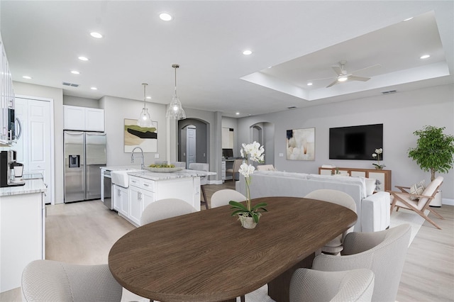 dining area featuring a raised ceiling, light hardwood / wood-style flooring, ceiling fan, and sink