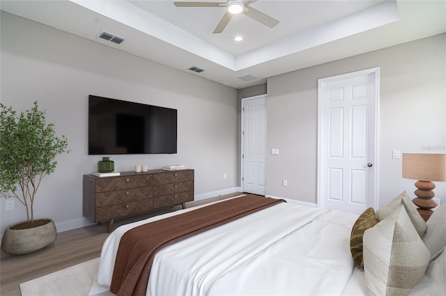 bedroom featuring ceiling fan, light wood-type flooring, and a tray ceiling