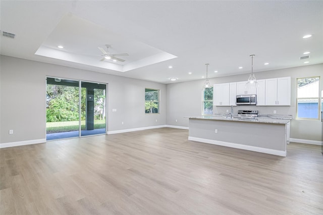 kitchen featuring white cabinetry, an island with sink, light hardwood / wood-style floors, decorative light fixtures, and appliances with stainless steel finishes