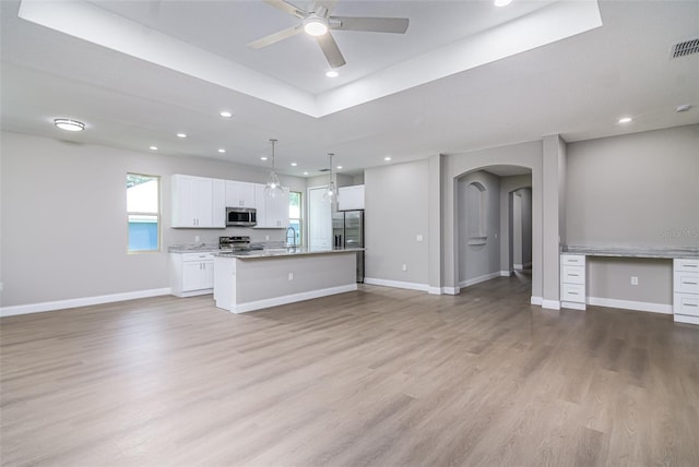 kitchen with white cabinetry, hanging light fixtures, a kitchen island with sink, appliances with stainless steel finishes, and light wood-type flooring