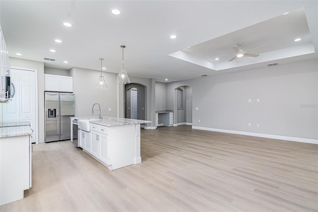 kitchen featuring appliances with stainless steel finishes, light wood-type flooring, white cabinetry, and a kitchen island with sink