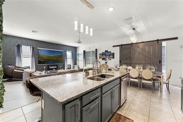 kitchen with a kitchen island with sink, sink, a barn door, decorative light fixtures, and plenty of natural light