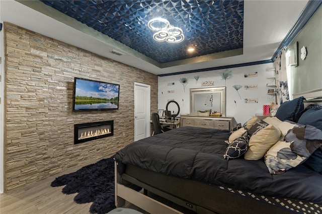 bedroom featuring hardwood / wood-style floors, a raised ceiling, and a stone fireplace