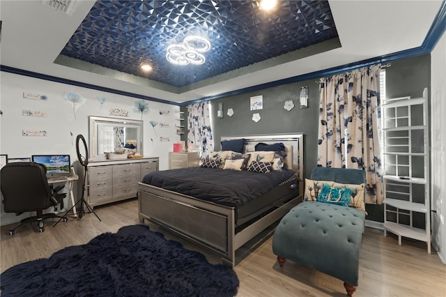 bedroom with light wood-type flooring, crown molding, and a tray ceiling