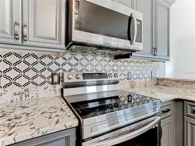 kitchen with gray cabinets, light stone countertops, stainless steel appliances, and backsplash