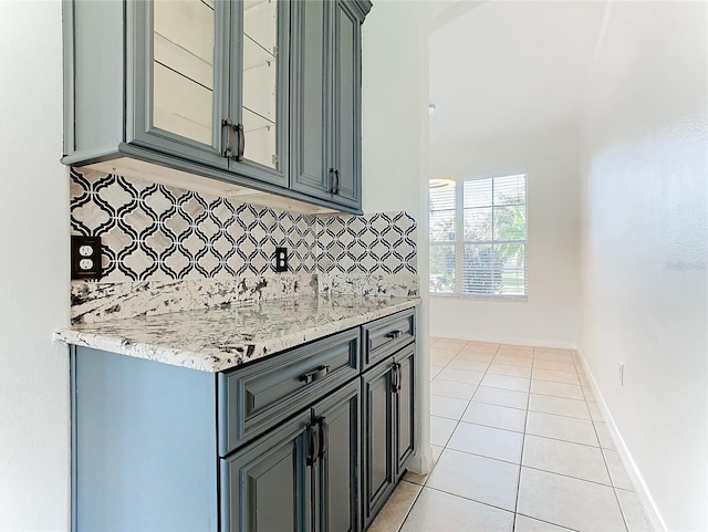 kitchen featuring gray cabinetry, backsplash, light stone countertops, and light tile patterned floors