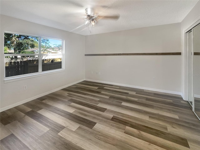 empty room with ceiling fan, a textured ceiling, and dark hardwood / wood-style flooring