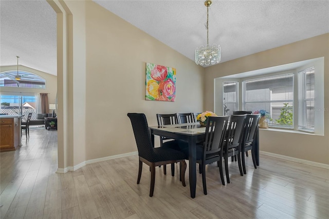 dining space featuring light hardwood / wood-style floors, a textured ceiling, vaulted ceiling, and an inviting chandelier