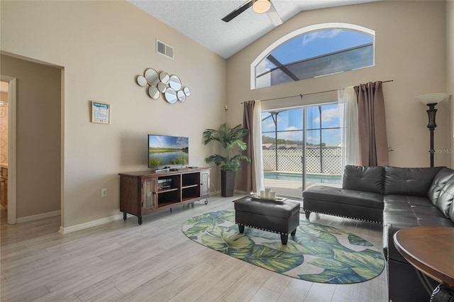 living room featuring light hardwood / wood-style flooring, a textured ceiling, high vaulted ceiling, and ceiling fan