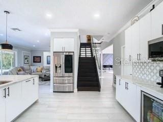 kitchen featuring light hardwood / wood-style floors, white cabinets, hanging light fixtures, stainless steel fridge with ice dispenser, and backsplash