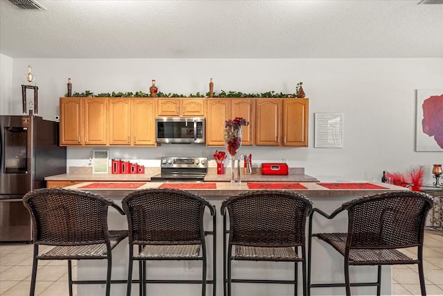 kitchen with light tile patterned flooring, sink, appliances with stainless steel finishes, a breakfast bar area, and a textured ceiling