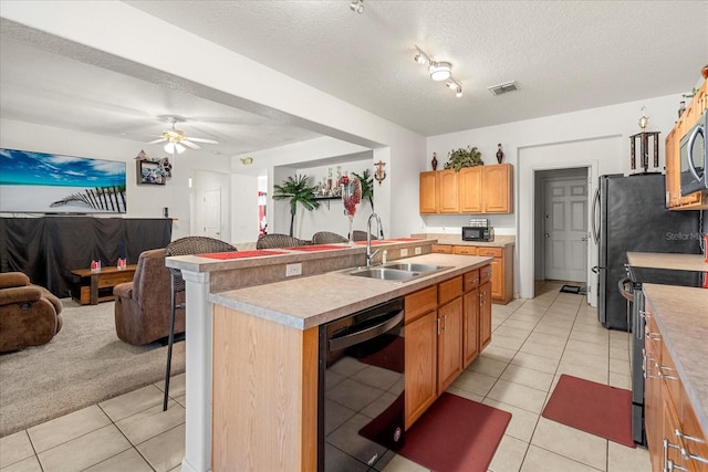 kitchen with stainless steel appliances, light colored carpet, a textured ceiling, sink, and a kitchen island with sink