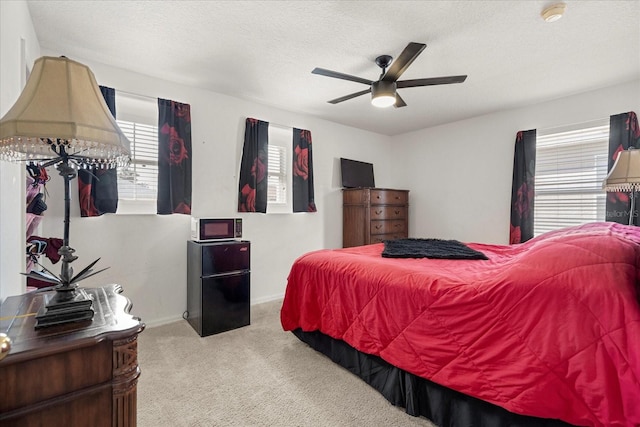 bedroom with a textured ceiling, light colored carpet, ceiling fan, and black refrigerator