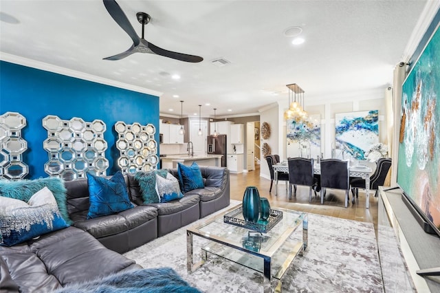 living room with ornamental molding, sink, light wood-type flooring, and ceiling fan