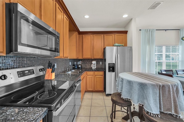 kitchen with appliances with stainless steel finishes, sink, backsplash, dark stone counters, and light tile patterned floors