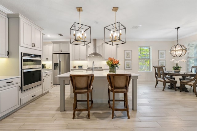 kitchen with a kitchen breakfast bar, stainless steel appliances, a kitchen island with sink, wall chimney range hood, and decorative light fixtures