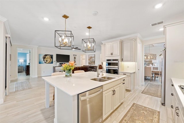 kitchen with pendant lighting, a kitchen island with sink, sink, light wood-type flooring, and appliances with stainless steel finishes