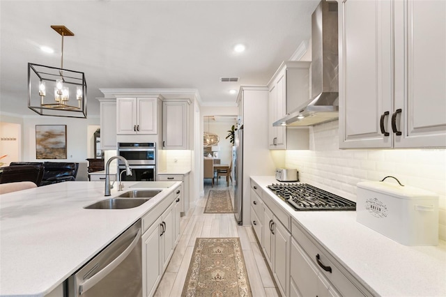 kitchen featuring wall chimney exhaust hood, stainless steel appliances, sink, pendant lighting, and an inviting chandelier