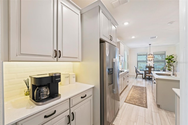 kitchen featuring sink, light hardwood / wood-style flooring, tasteful backsplash, decorative light fixtures, and stainless steel fridge with ice dispenser