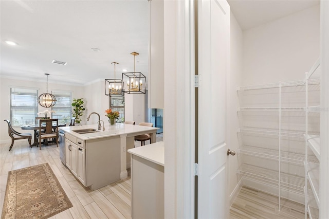 kitchen with sink, hanging light fixtures, light hardwood / wood-style flooring, stainless steel dishwasher, and a center island with sink