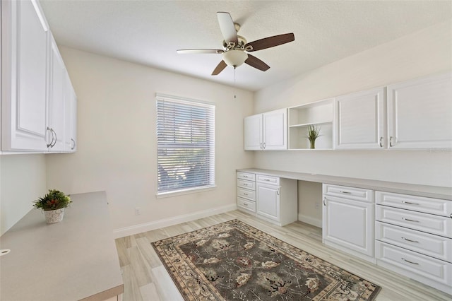 office space featuring light wood-type flooring, a textured ceiling, built in desk, and ceiling fan