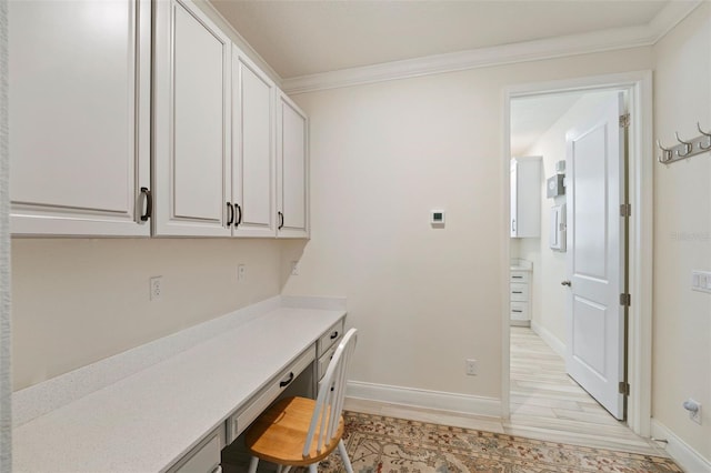 office space featuring built in desk, light wood-type flooring, and ornamental molding