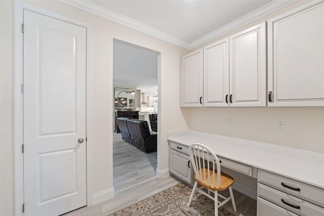 office space featuring crown molding, built in desk, and light wood-type flooring