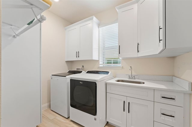 laundry area featuring washer and dryer, cabinets, sink, and light hardwood / wood-style flooring