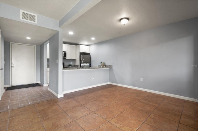 kitchen with white cabinets, light stone counters, kitchen peninsula, stainless steel appliances, and tile patterned floors