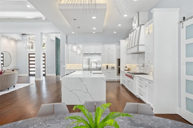 kitchen with dark wood-type flooring, a large island with sink, white cabinetry, and a barn door