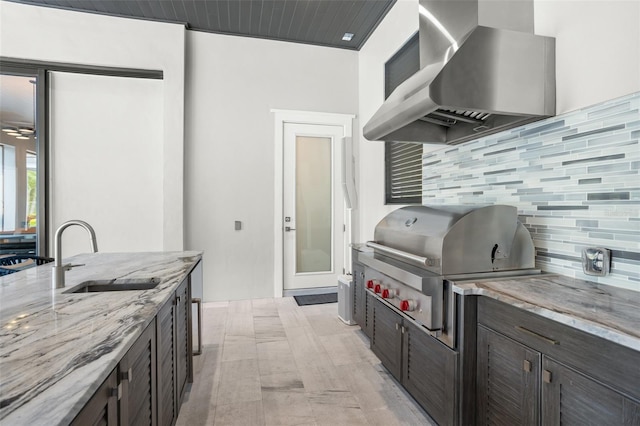 kitchen with light stone counters, sink, decorative backsplash, and wall chimney range hood