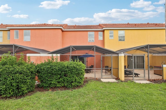 back of house with a patio, glass enclosure, and a lawn