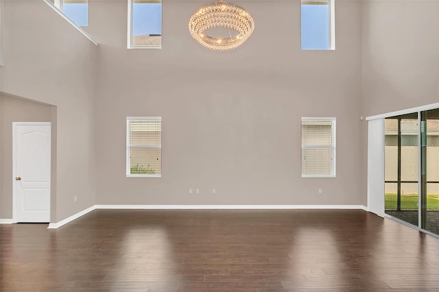 unfurnished living room with an inviting chandelier, a high ceiling, and dark hardwood / wood-style floors