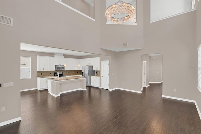 unfurnished living room featuring a towering ceiling, dark hardwood / wood-style flooring, and a chandelier