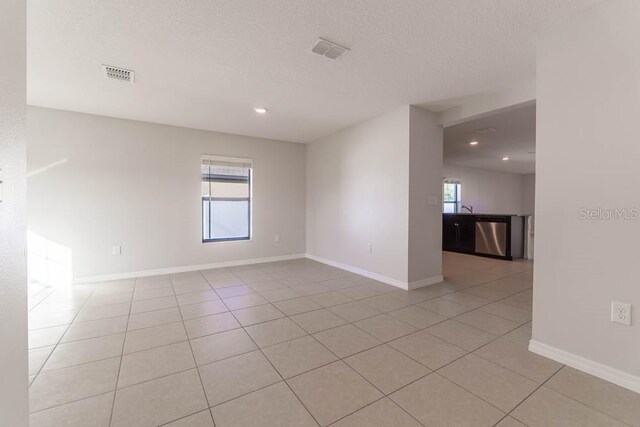 spare room featuring sink, a textured ceiling, and light tile patterned floors